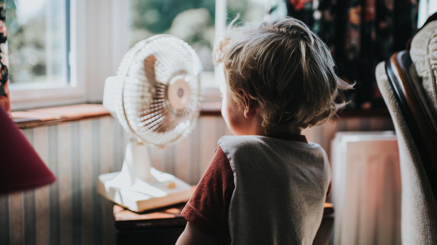 A boy standing in front of a fan