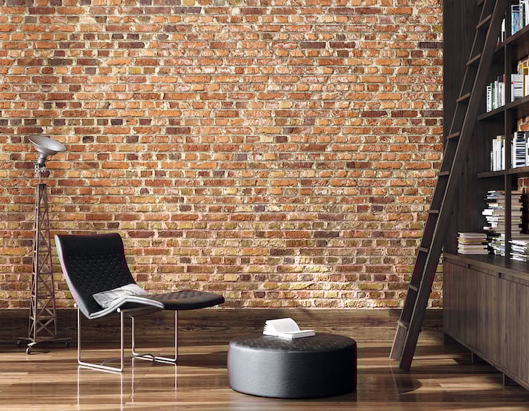 a brick wall and wood floor room with black modern reading chair and lamp, ottoman, and bookshelf with ladder