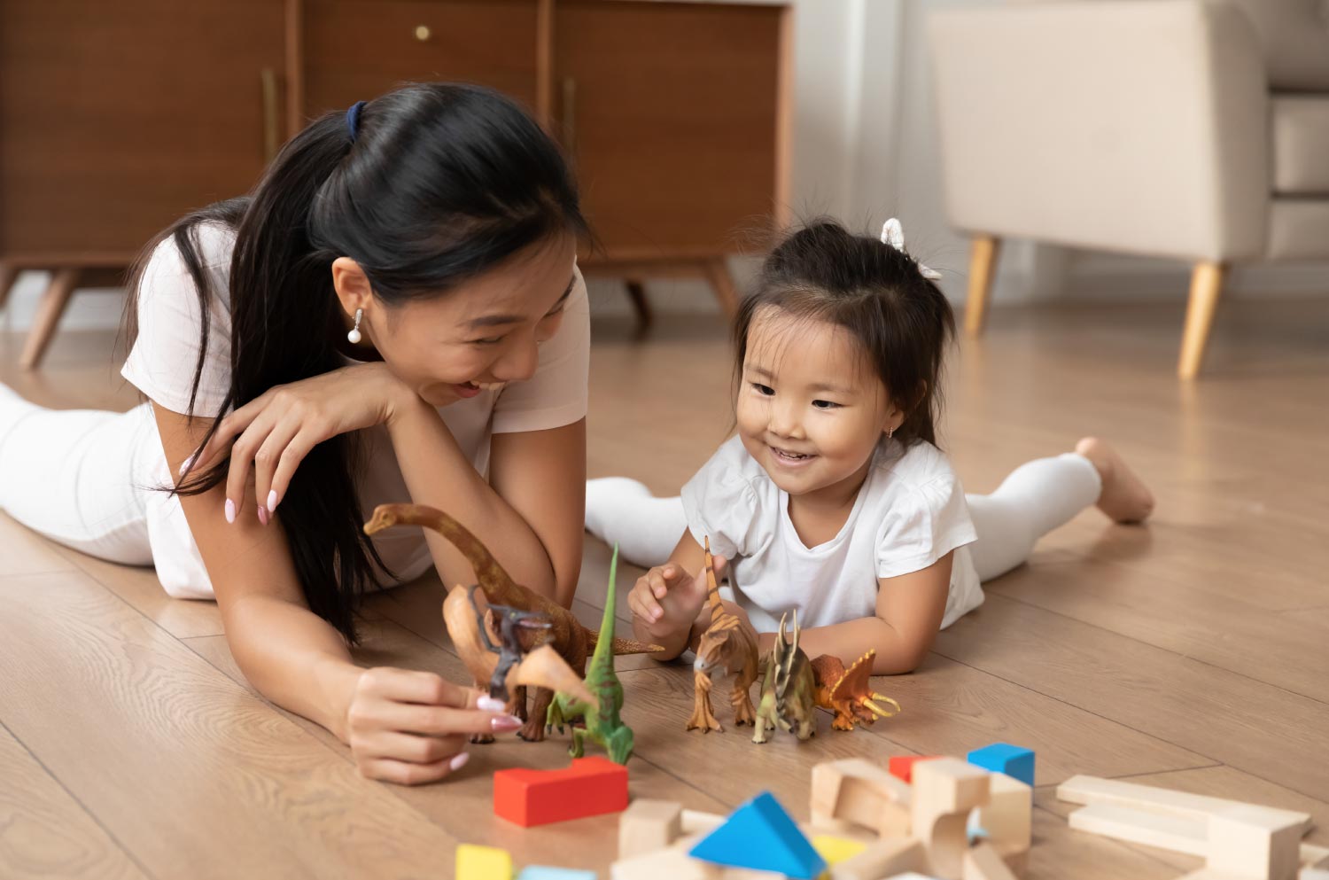 Mom plays dinosaurs with toddler laying on floor