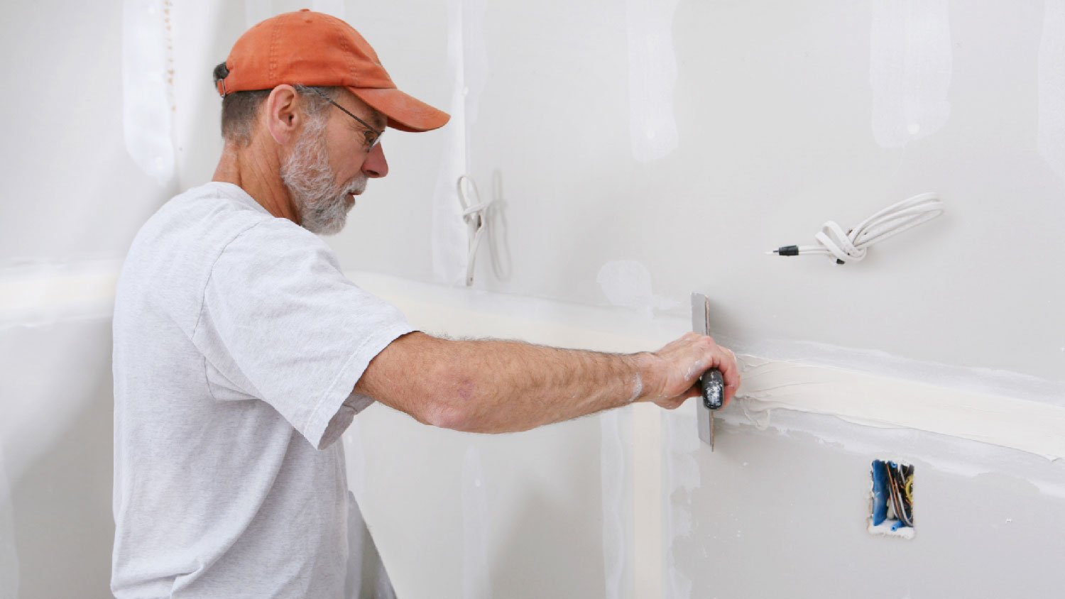 A senior man applying spackle on wall